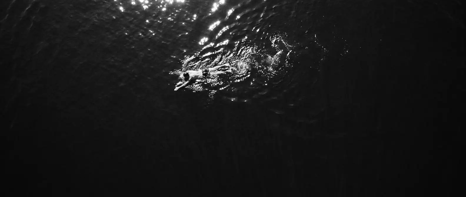 Aerial view of a lone open-water swimmer in a vast ocean, representing brand knowledge and visibility management