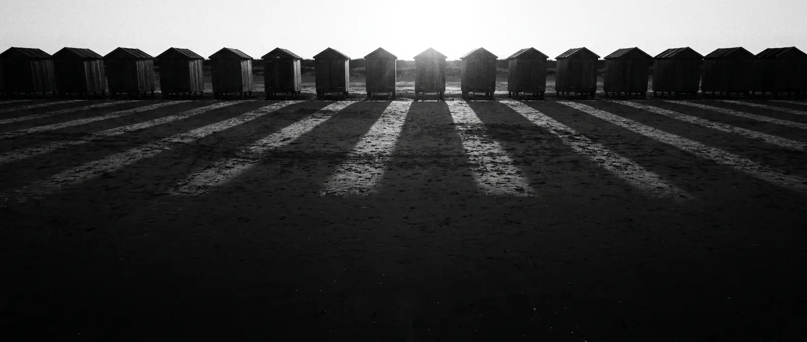 Long identical row of beach bathing boxes casting matching shadows, representing digital presence consistency